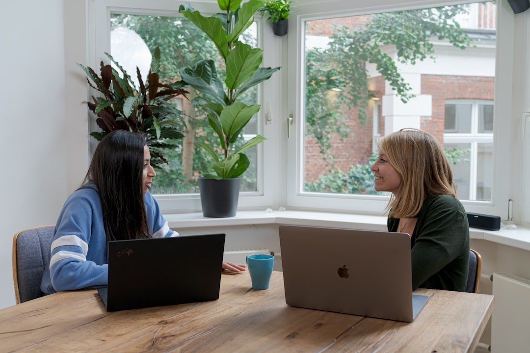Zwei Frauen besprechen sich an einem Tisch mit Laptops.
